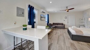 Een moderne woonkamer met een bank, een eethoek met een tafel, en een bed met plafondventilator.