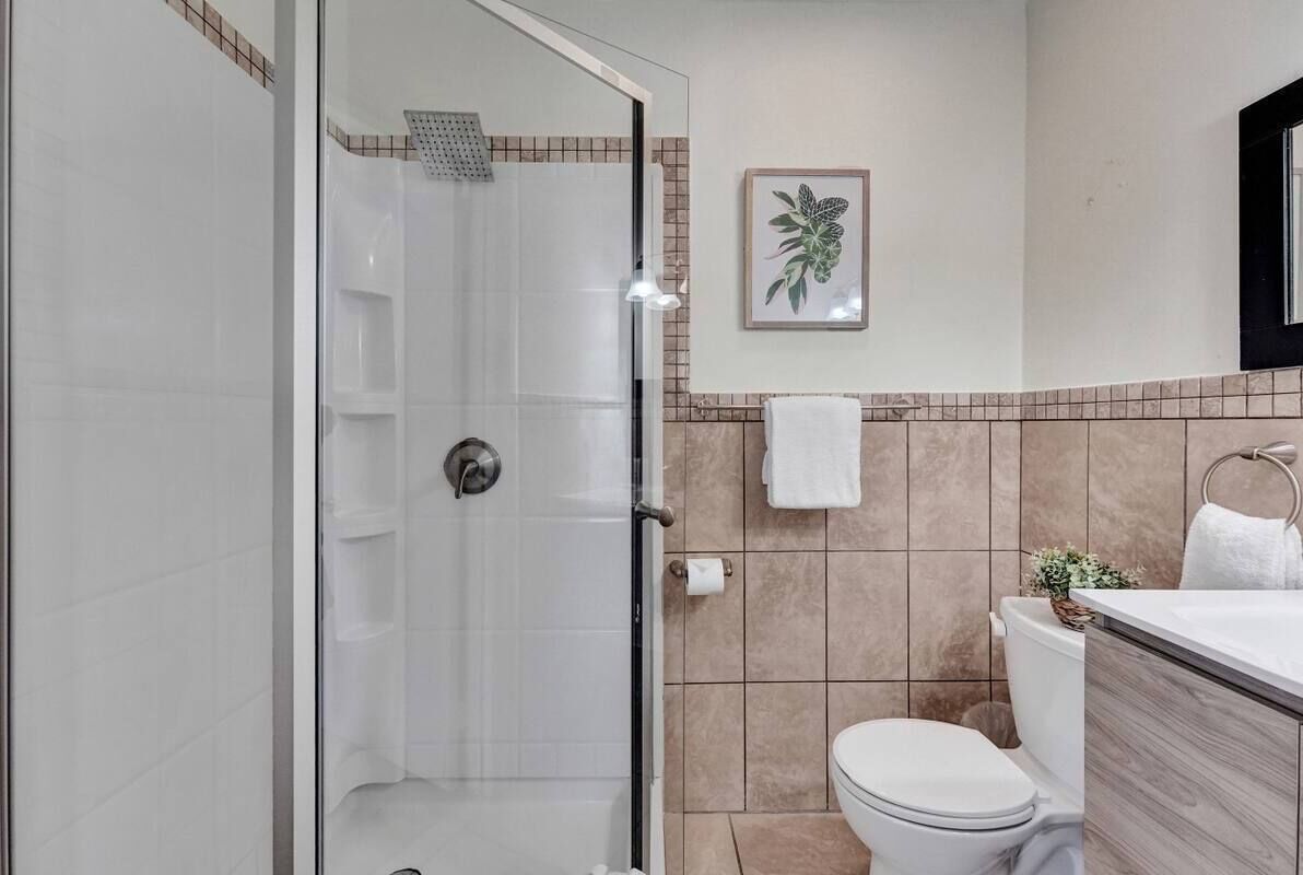 A bathroom with a glass-enclosed shower, a white toilet, and a sink with a mirror.