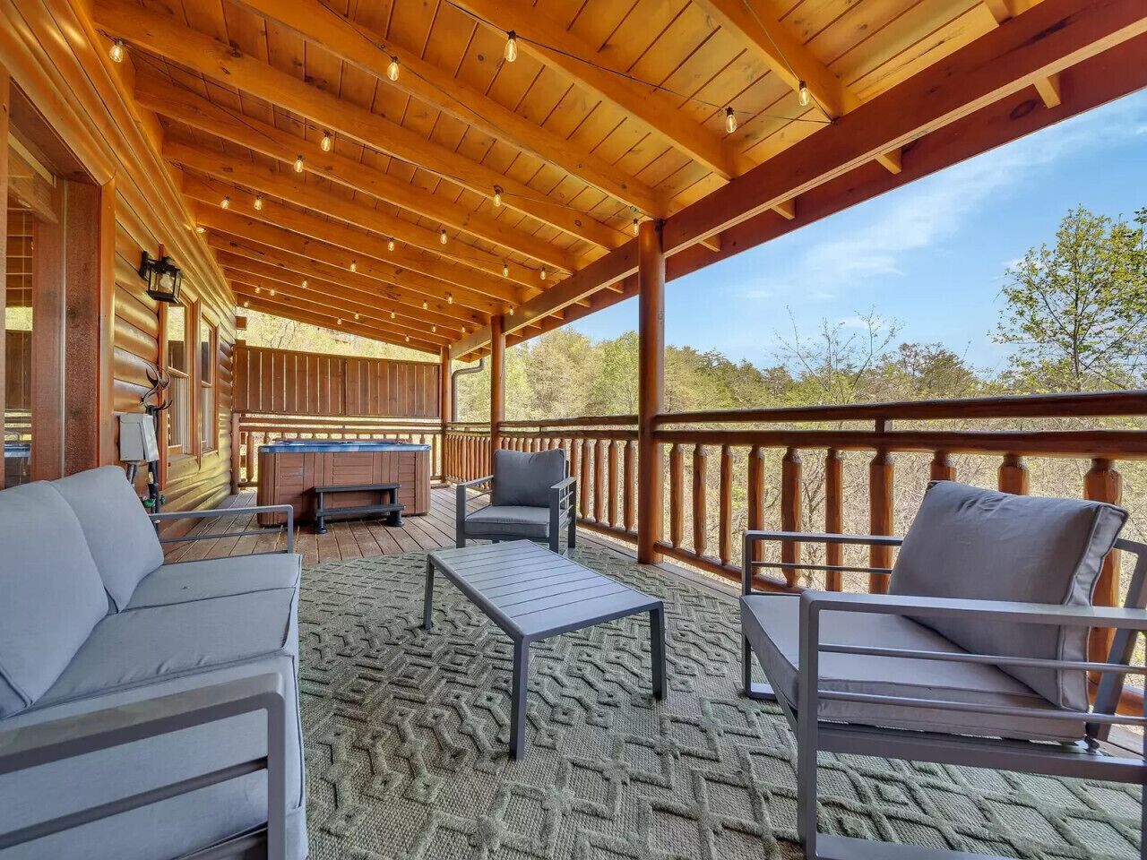A covered outdoor seating area with a wooden ceiling, a sofa, two chairs, and a small table.