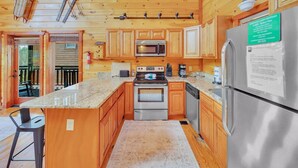 A wooden cabin interior with a kitchen featuring wooden cabinets, a stainless steel refrigerator, a microwave, an oven, and a sink. - Rustic Retreat – Jacuzzi, Fireplaces & Views (Sevierville)
