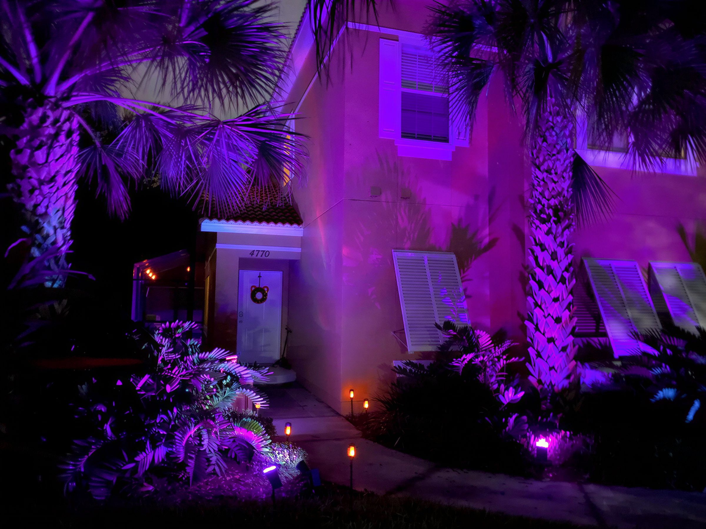 A house with a number 4770 on the door, surrounded by palm trees and illuminated by purple lighting.