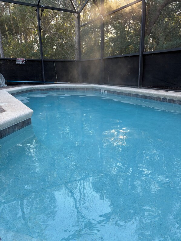 A clear blue pool with a safety sign, surrounded by a metal fence and trees.