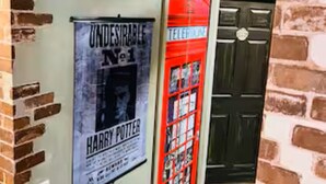 Een bakstenen muur met een poster van een Harry Potter boek en een rode boekenkast.