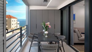 Ein Balkon mit Tisch und Stühlen, einer Blumenvase und Blick auf Gebäude und das Meer.