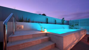 Ein moderner Poolbereich im Freien mit Treppen zu einem beheizten Pool, umgeben von einer niedrigen Mauer und Pflanzen.