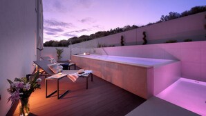 Eine Terrasss mit integriertem Whirlpool, Liegestühlen und einem kleinen Tisch, auf dem ein Hut und Blumen liegen.