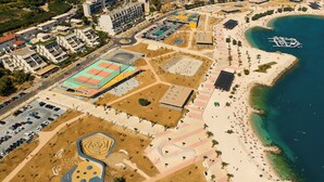 Luftaufnahme einer Küstenregion mit Strand, Parkplatz und Sportkomplex.