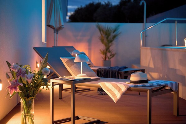 Un área de descanso al aire libre iluminada por el sol, con una mesa, sillas y un jarrón de flores.
