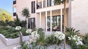 A modern building with a patio area featuring outdoor seating and a garden with various plants and flowers. - Qumi Porto Suites (Tivat)