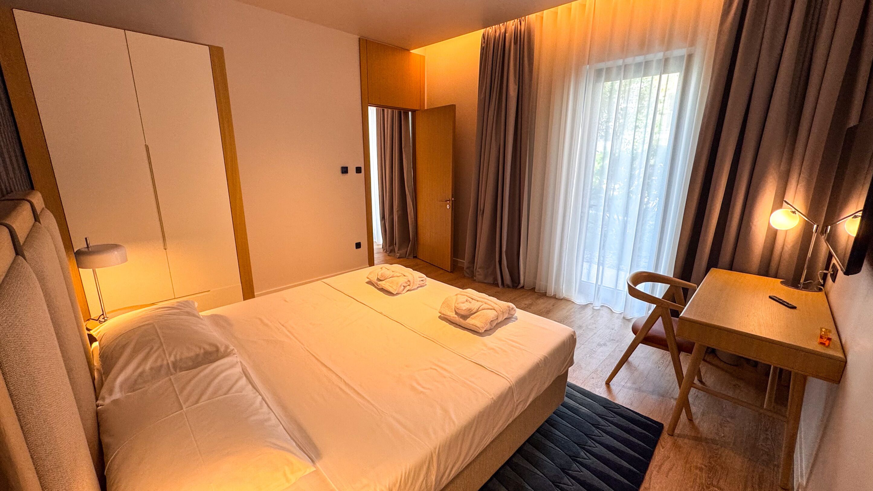 A hotel room with a bed, a desk, a chair, and a window with curtains.