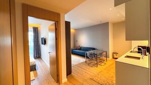 A modern apartment with a wooden floor, a glass dining table, a sofa, and a kitchen area with a sink and countertop. - Qumi Porto Suites (Tivat)