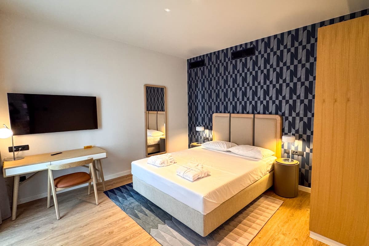 Une chambre d’hôtel moderne équipée d’un lit, de tables de chevet, d’un bureau et d’une télévision.