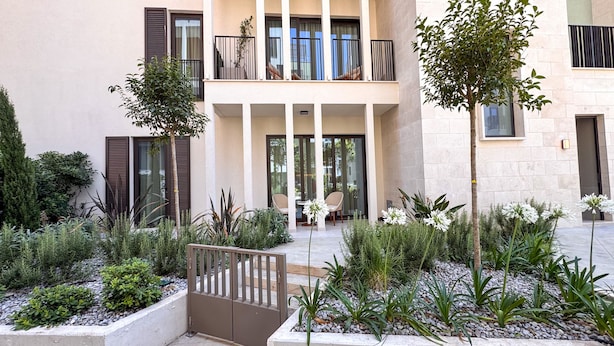 A modern building with a courtyard featuring a seating area, plants, and a gated entrance. - Qumi Porto Suites (Tivat)