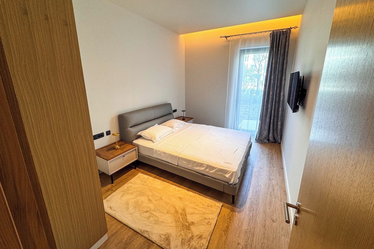 Une chambre à coucher moderne avec un lit, une table de chevet et une vue sur l’extérieur par une fenêtre.