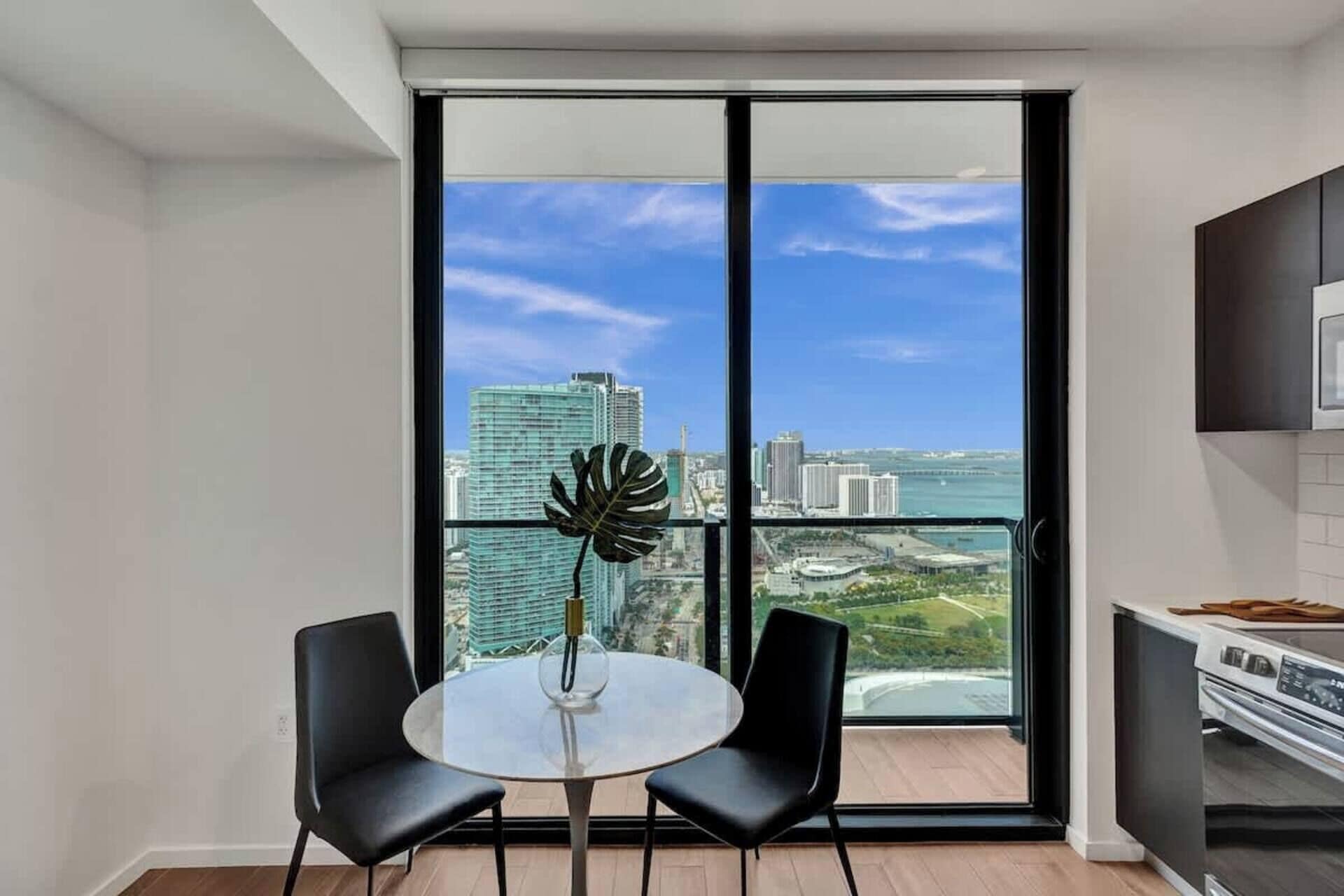 Um apartamento moderno com varanda, uma mesa de jantar com duas cadeiras e uma área de cozinha.
