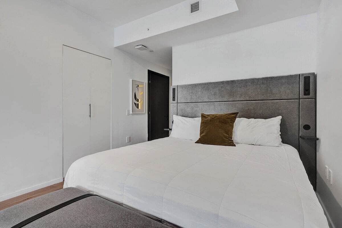 Una habitación de hotel moderna con una cama grande, un cabecero gris y una pared blanca.