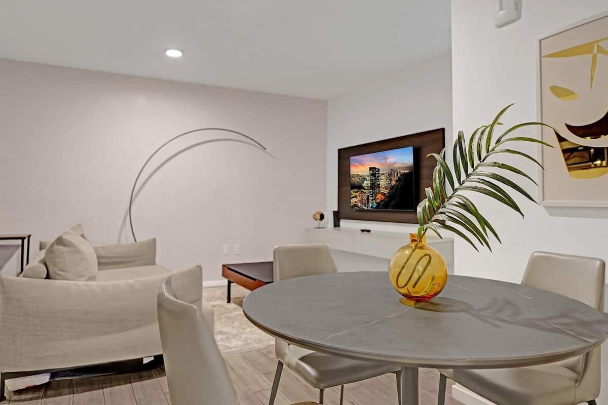 Una sala de estar moderna con una mesa redonda, un sofá, un televisor de pantalla plana y una planta.