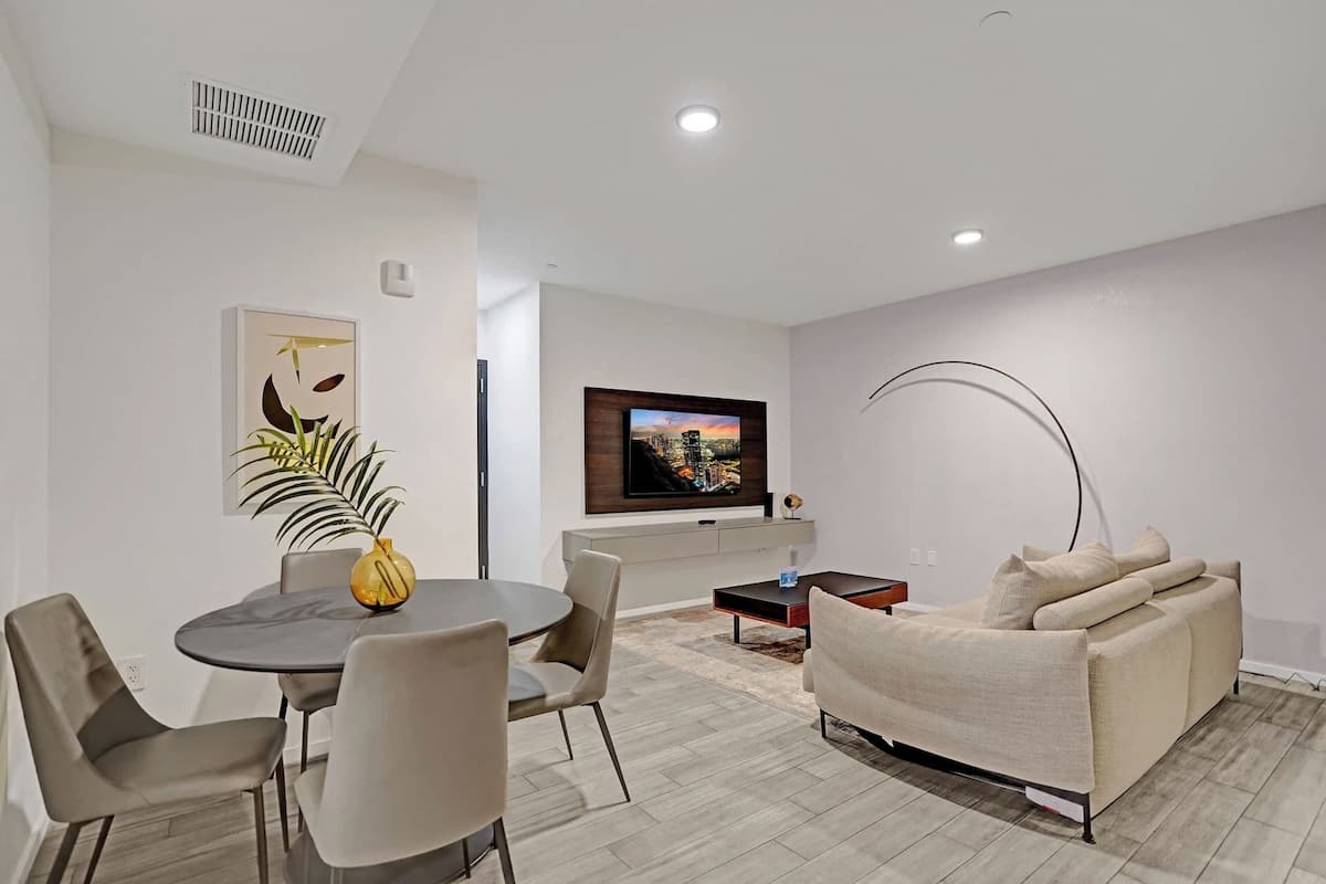 Una sala de estar moderna con comedor, sofá, televisor y una obra de arte original en la pared.