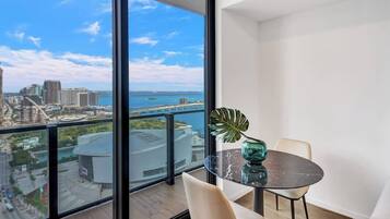 En balkon med udsigt over by og vand, et bord med glasplade og en enkelt stol.