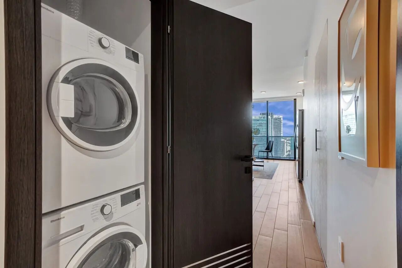 A modern laundry room with stacked washing machines and a dark door leading to a balcony with a city view.