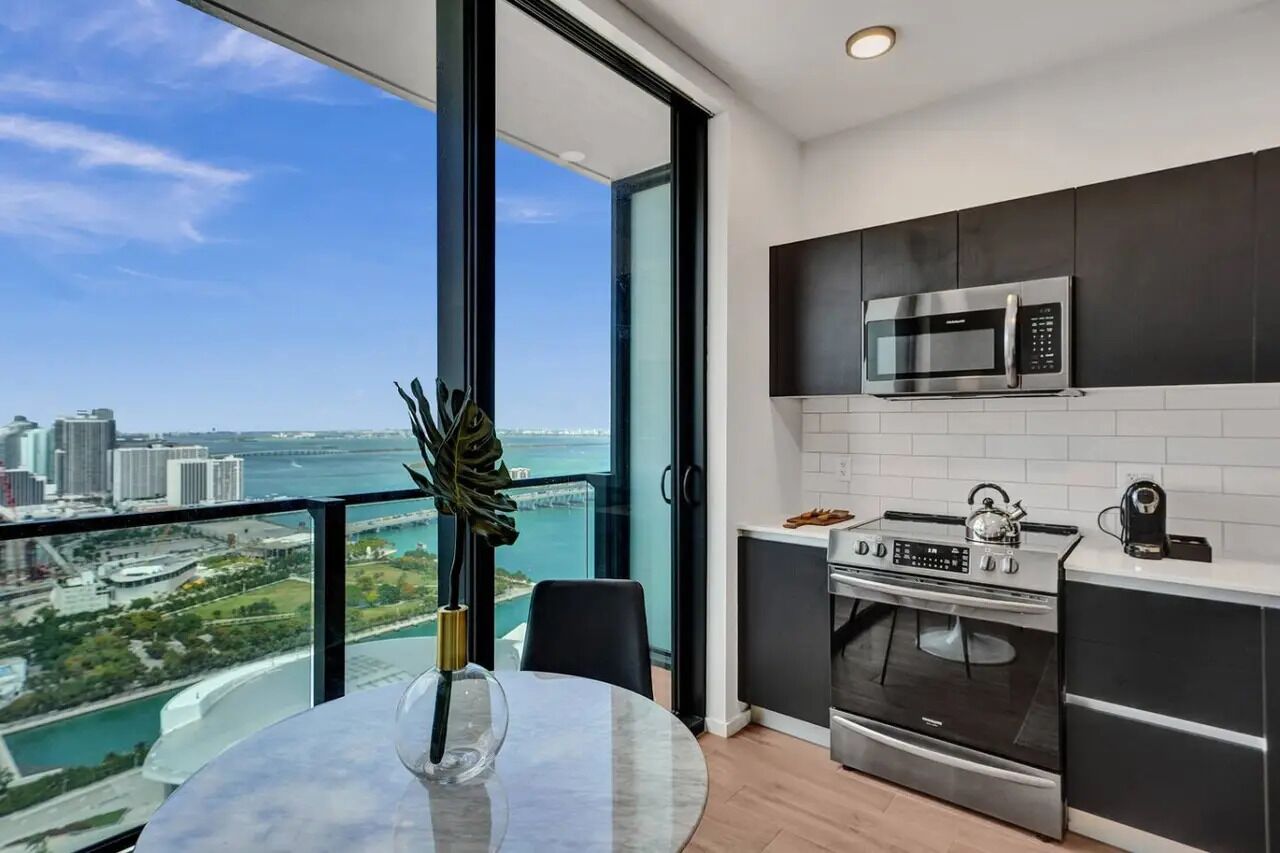 Uma cozinha moderna com uma janela grande, vista da cidade e área de jantar com mesa e cadeiras.