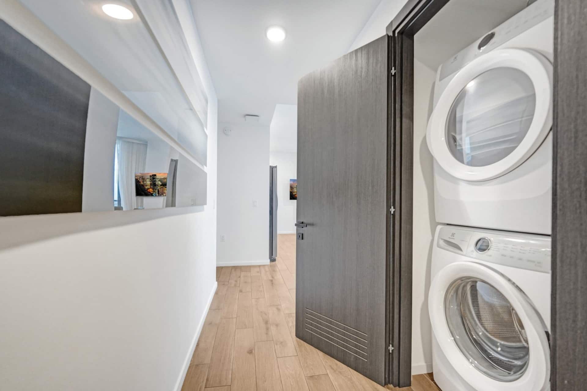 A laundry room with two front-loading washing machines, a wooden floor, and a door leading to another room.