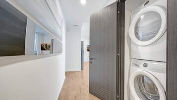 A laundry room with two front-loading washing machines, a wooden floor, and a door leading to another room.