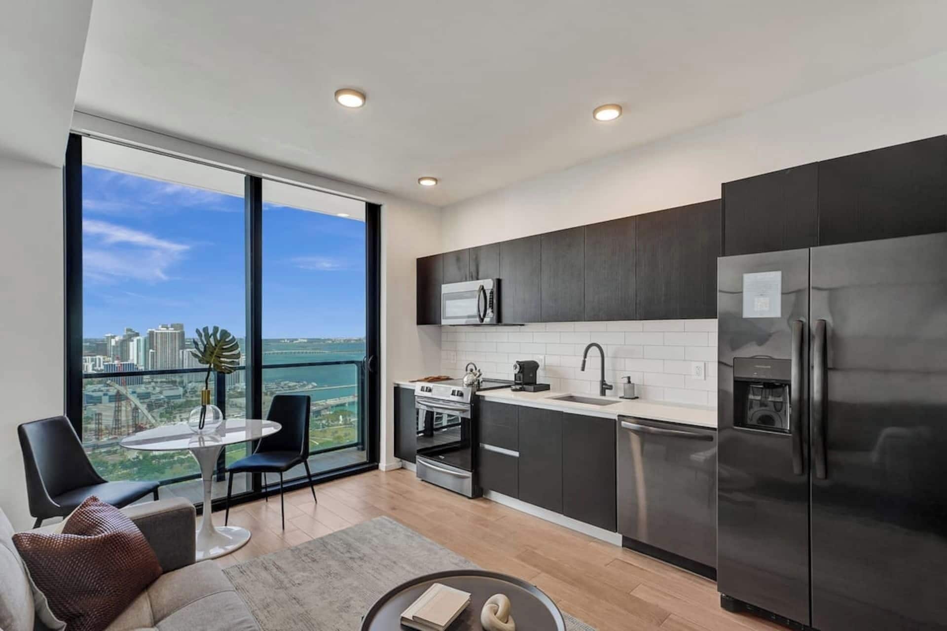 A modern kitchen with a large window, a dining area, and a view of a cityscape.