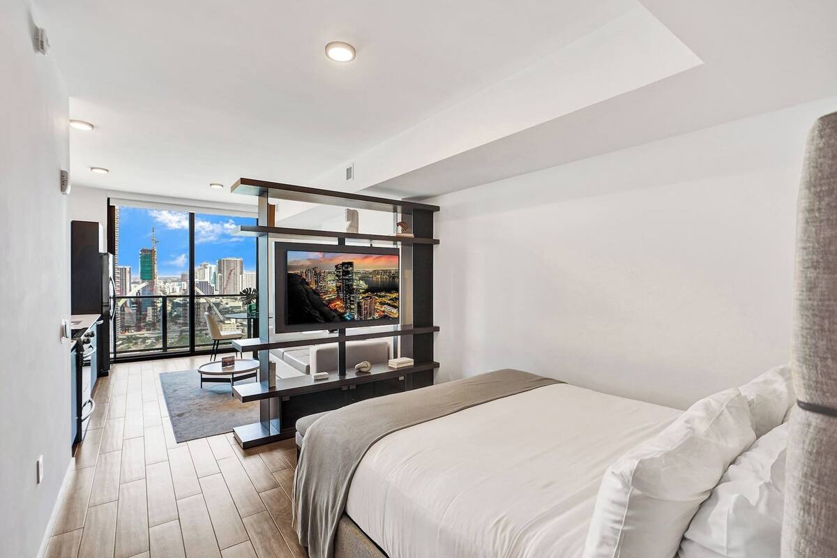Un dormitorio moderno con vistas a la ciudad, televisión de pantalla plana y balcón con paisaje urbano.