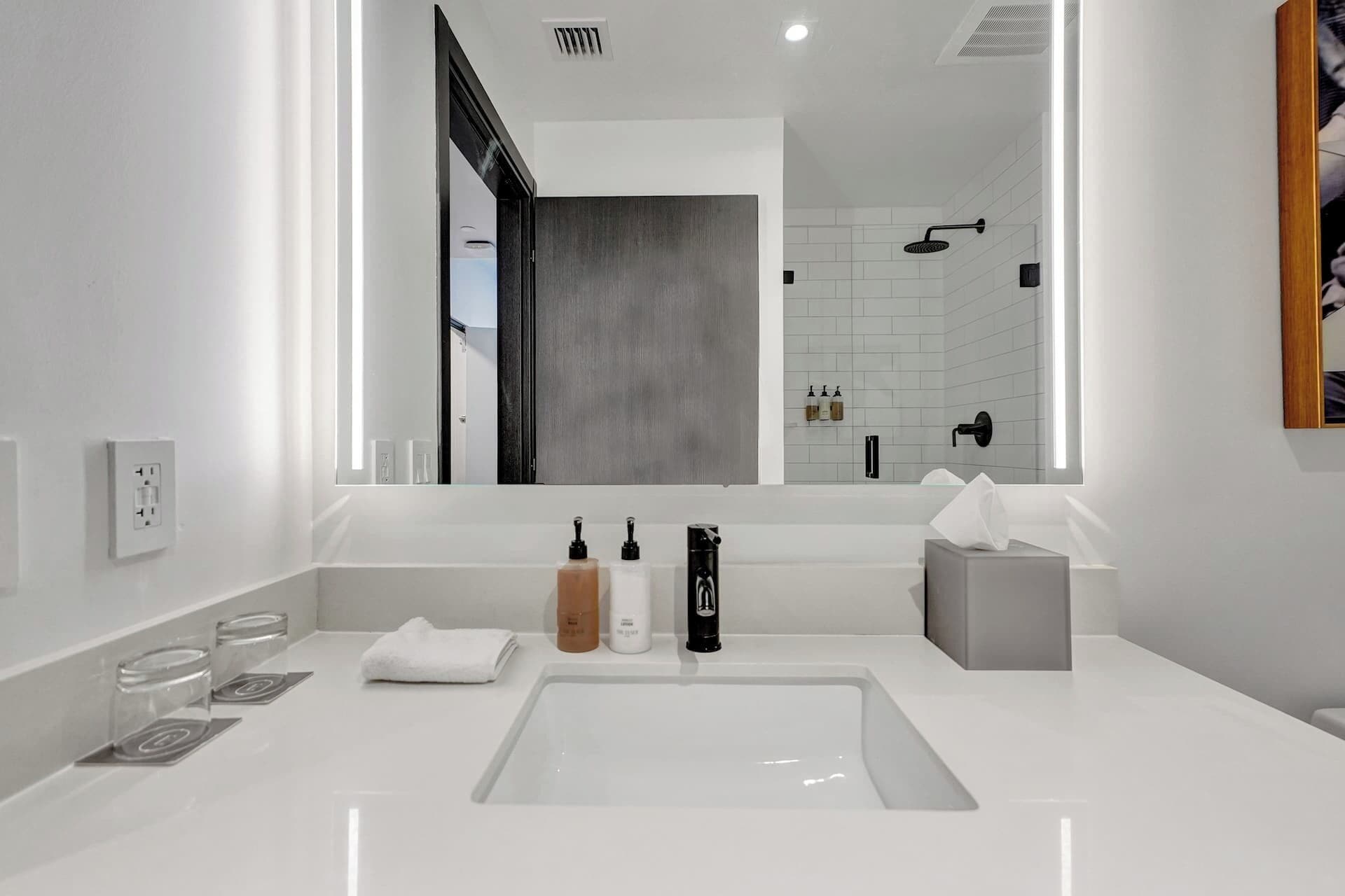 A modern bathroom with a large mirror, white sink, and a shower area visible in the background.