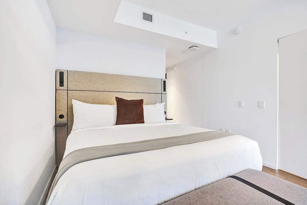 Una habitación de hotel moderna con una cama grande, un cabecero y una mesita de noche pequeña.