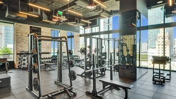 A gym with weightlifting equipment, large windows, and a view of buildings.