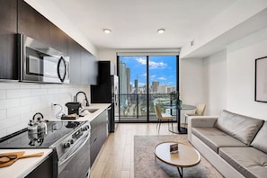 A modern kitchen with a stove, microwave, and sink, a balcony with a city view, a sofa, and a small table.