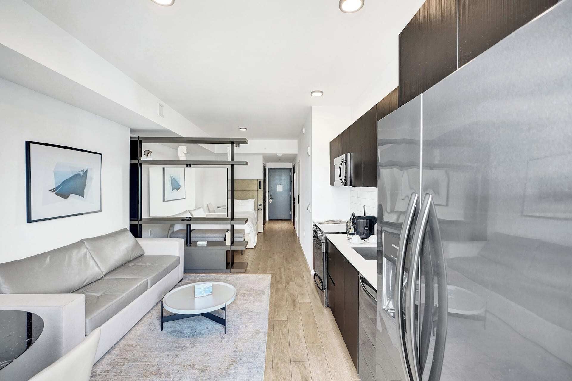 A modern kitchen with a refrigerator, a dining area with a table and chairs, and a living room with a sofa and a coffee table.