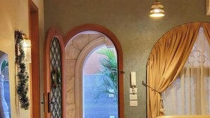 A hotel lobby with a beige sofa, a small round table, and a decorative archway leading to a balcony with a view of a palm tree. - 2BRs Garden side view-Three Sisters Villa 2 (New Cairo City)