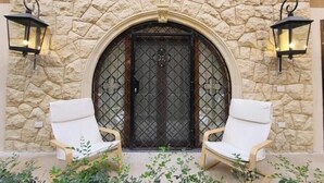 A stone wall entrance with a metal gate, two white chairs, and two wall-mounted lanterns. - 6BRs with private entrance -Three Sisters Villa (New Cairo City)