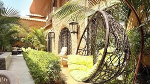 A patio area with a hanging chair, a small table, and a pathway leading to a building with arched windows and a stone facade. - 6BRs with private entrance -Three Sisters Villa (New Cairo City)