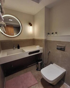 A modern bathroom with a round mirror, a sink, a toilet, and a shower.