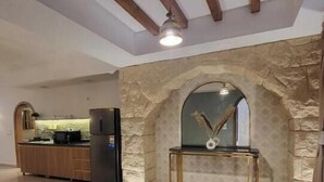 Amplia sala de estar con un arco de piedra, un tapete redondo y una cocina al fondo.