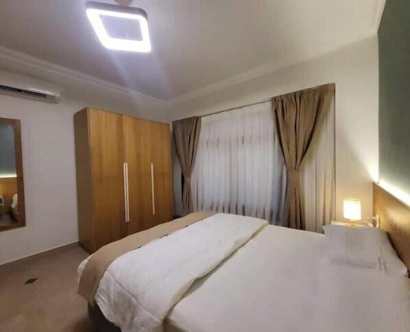 Une chambre d’hôtel avec un lit, une armoire, des rideaux et une lampe de chevet.