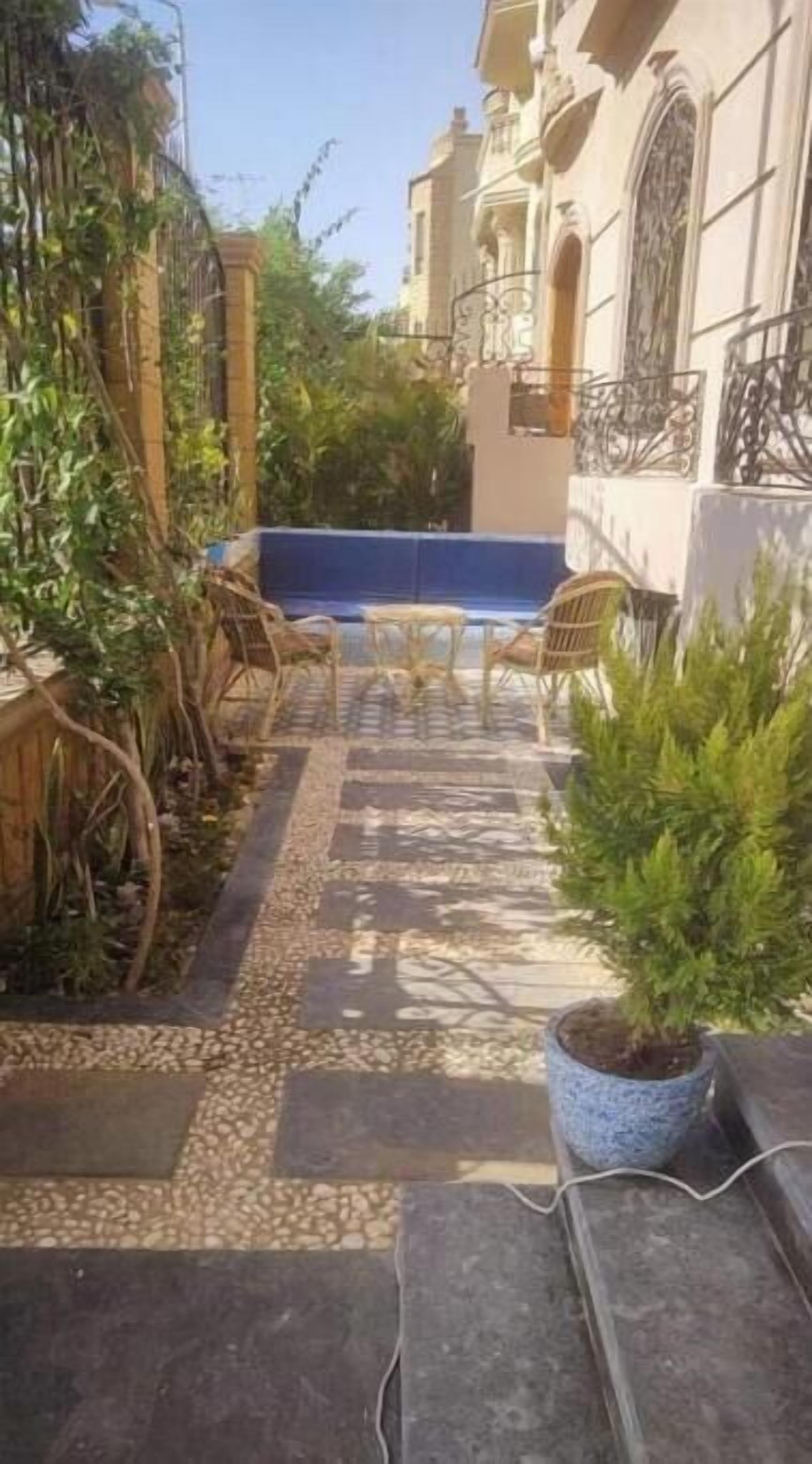 A courtyard with a blue pool, wicker chairs, and potted plants.