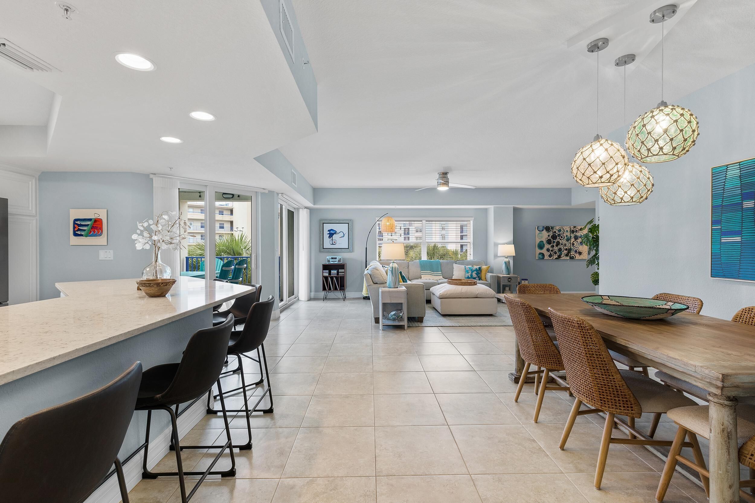 A spacious kitchen with a large island, modern bar stools, and a dining area with a wooden table and wicker chairs.