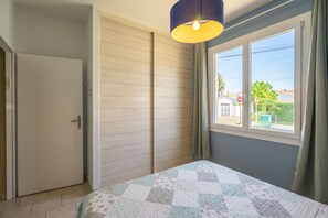 Um quarto com cama, janela com cortinas, porta e luminária suspensa.