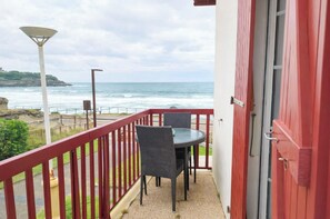 A balcony with a table and chairs, overlooking the ocean with a red railing.