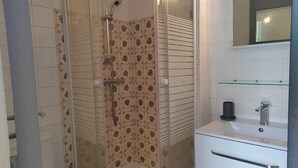 A bathroom with a glass-enclosed shower, a white sink with a mirror above it, and a patterned tile backsplash. - Studio with a beautiful view of the sea of Anglet (Anglet)