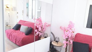 A bedroom with a red bed, a mirror, pink flowers, and a small round table with a lamp. - Studio with a beautiful view of the sea of Anglet (Anglet)