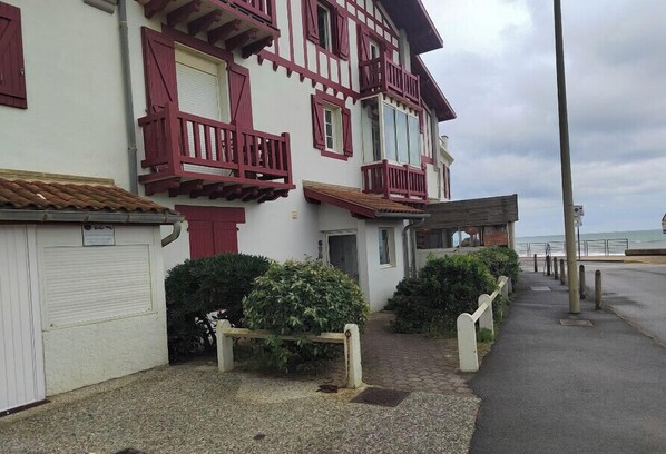 A traditional building with a balcony, a garage, and a pathway leading to the sea.