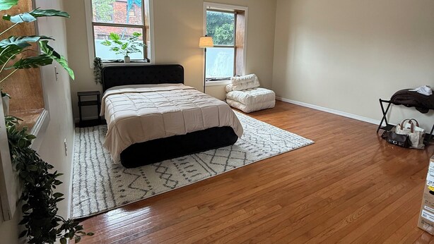 A spacious bedroom with a large bed, two windows, a ceiling fan, and a wooden floor.
