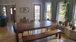 A spacious dining area with a wooden table and benches, a ceiling fan, and large windows with potted plants. - Spacious 5-bedroom House, Walking Distance to Williams (Williamstown)