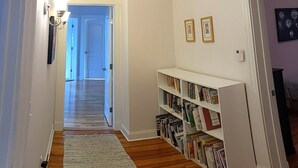 A hallway with wooden flooring, a white rug, and a bookshelf filled with books. - Spacious 5-bedroom House, Walking Distance to Williams (Williamstown)